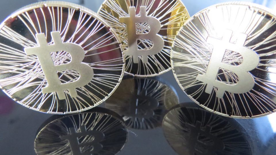 Three physical bitcoin coins standing on a reflective black surface