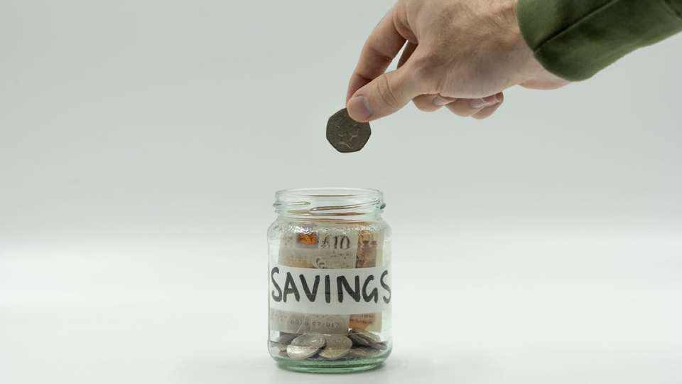 A coin dropped into a jar labelled savings